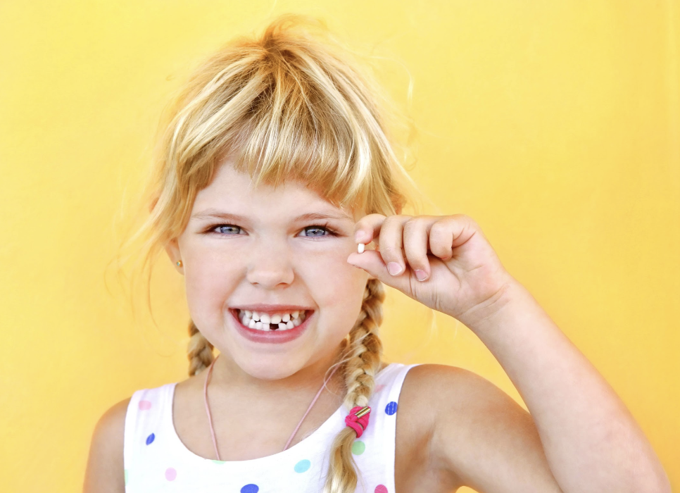 little girl smiling while holding tooth 