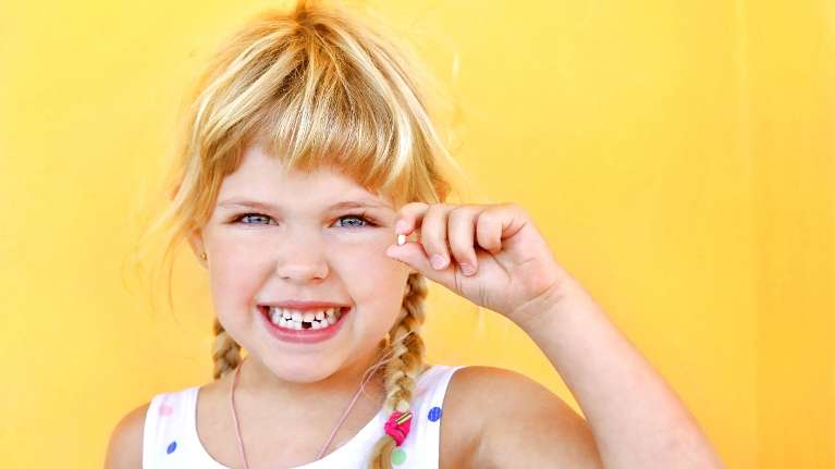 young girl holding her baby tooth after she lost it