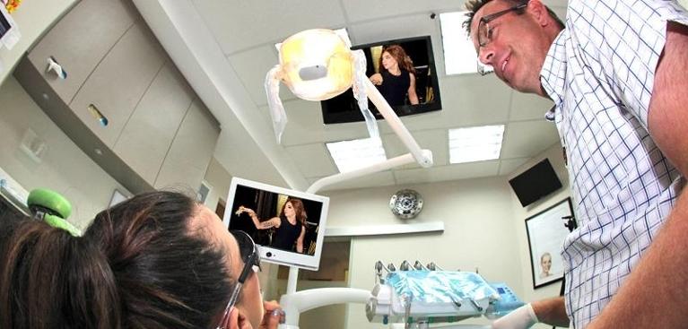 TVs above dental chairs with Dr Duke standing next to patient